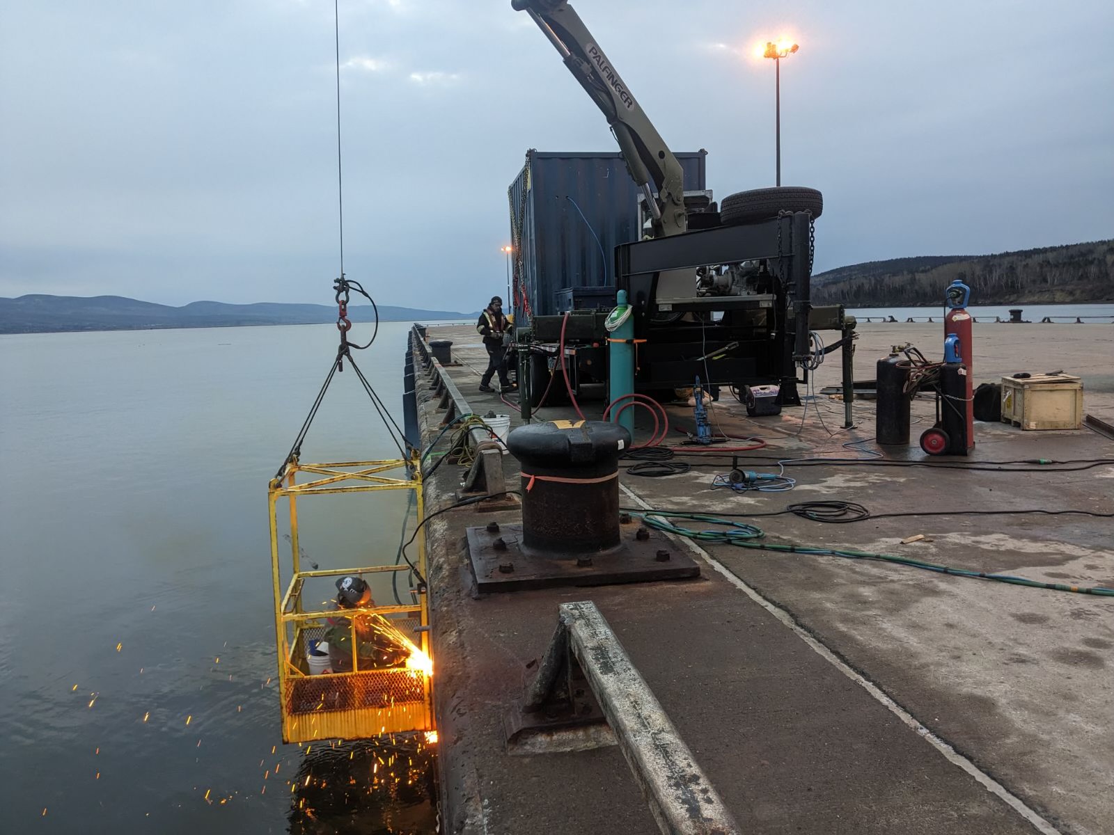 Mobile welding unit at an industrial dockside job site, with crane and container